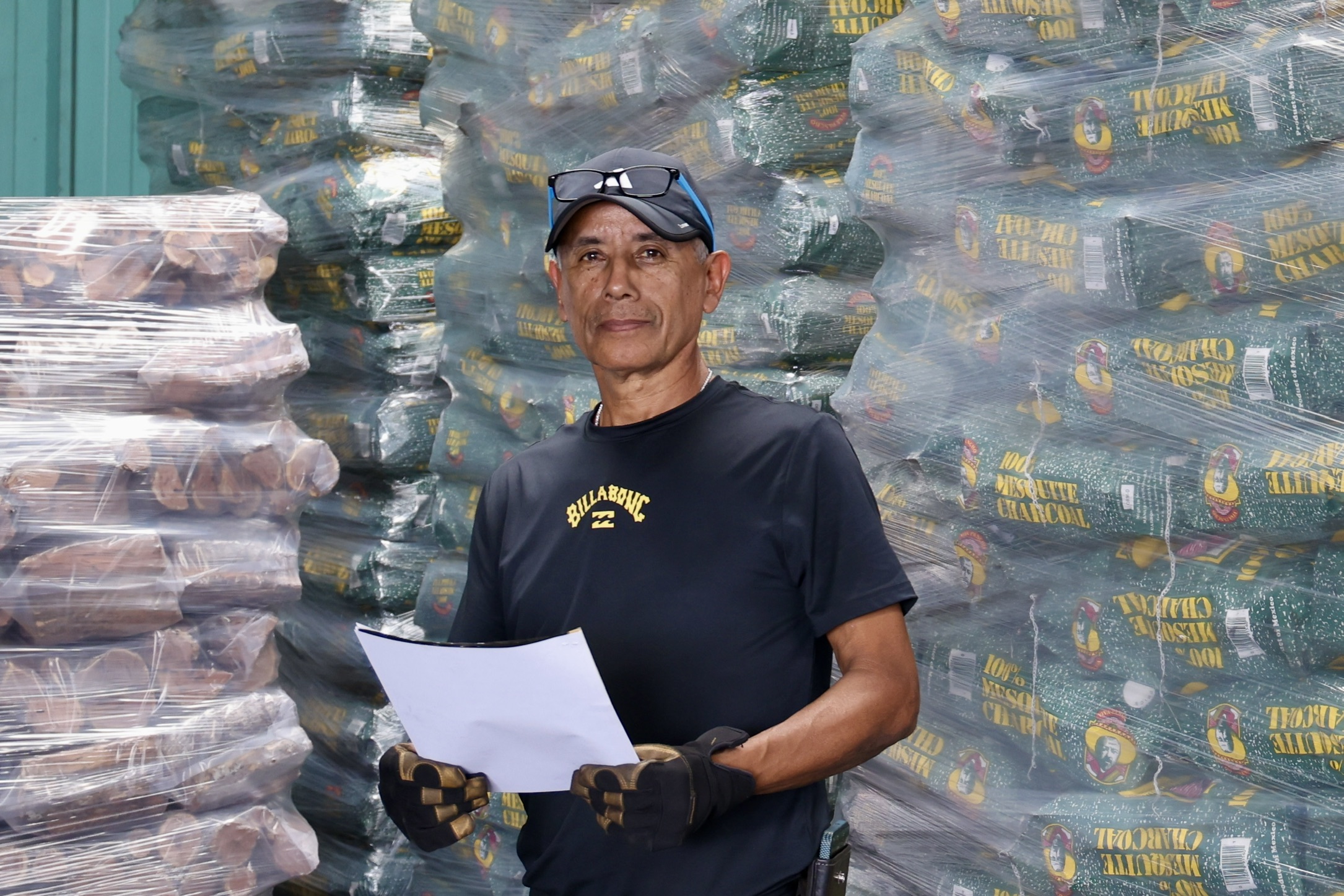 Raul standing in front of stacked pallets of Viva Pancho mesquite charcoal